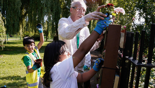 A man helping two children in the garden.